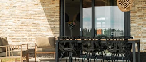 An outdoor seating area with a brick wall, a wooden table, and black chairs.