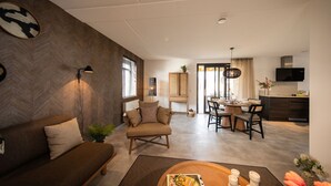 A modern living room with a sofa, a chair, a dining area with a table and chairs, and a kitchen area with a TV and cabinets. - Harbor View 4p - Two Bedroom Villa, Sleeps 4 (Thorn)