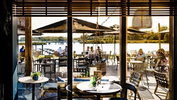 An outdoor dining area with tables and chairs, umbrellas, and a view of a lake. - Harbor View 4p - Two Bedroom Villa, Sleeps 4 (Thorn)