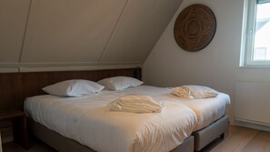 A neatly made bed in a room with a sloped ceiling, a round wall decoration, and a window. - Premium Game 12p - Six Bedroom Villa, Sleeps 12 (Thorn)
