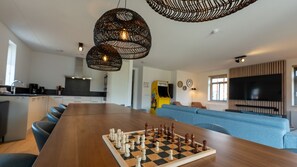 A modern living space with a wooden dining table set for a game of chess, a kitchen area, and a seating area with a large flat-screen TV. - Premium Game 12p - Six Bedroom Villa, Sleeps 12 (Thorn)