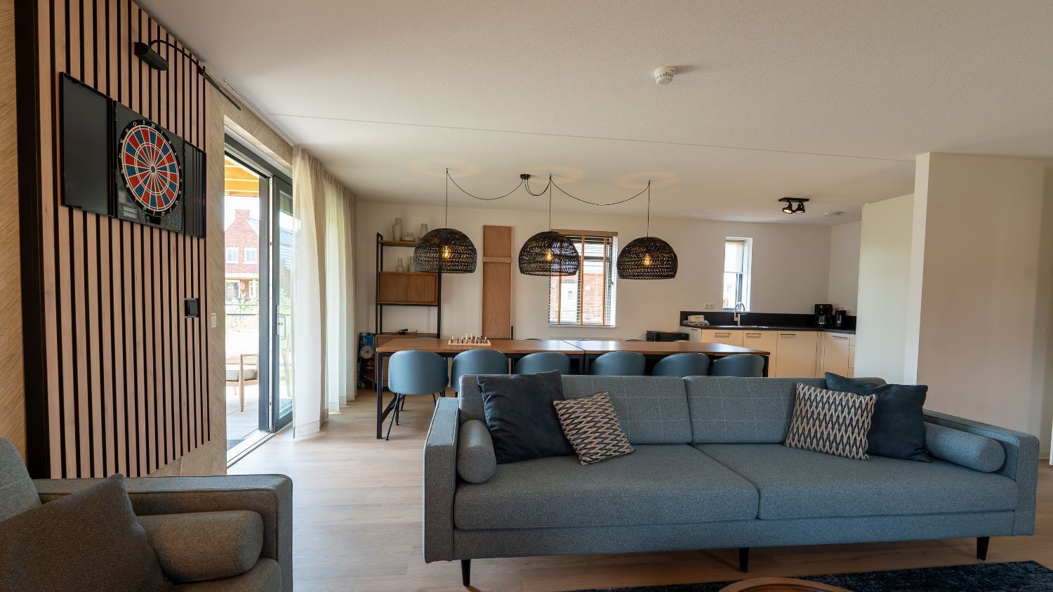 Una sala moderna con un sofá gris, un comedor con sillas azules y una cocina al fondo.