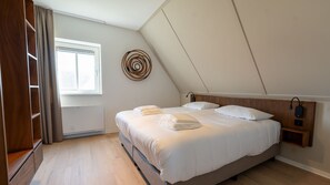 Een slaapkamer met een bed, een nachtkastje, een lampje aan de muur en een raam met gordijnen.