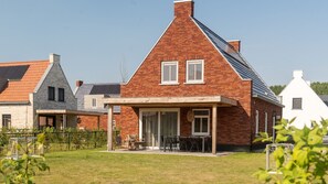 A residential building with a brick exterior, a covered patio with outdoor furniture, and a clear sky.