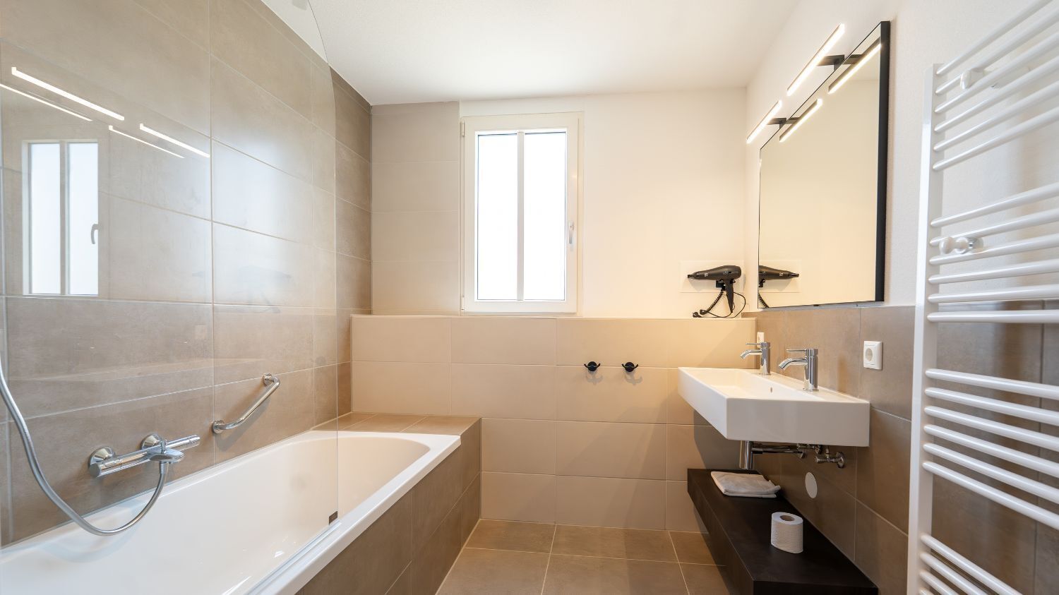 A modern bathroom with a bathtub, a sink, a mirror, and a towel rack.
