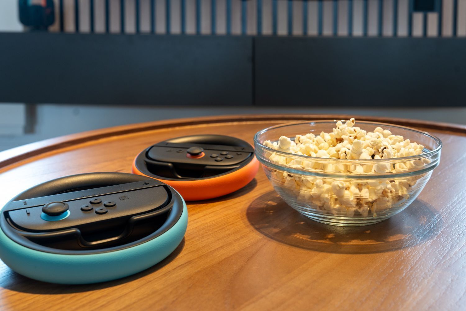 Three gaming controllers on a wooden table with a bowl of popcorn.