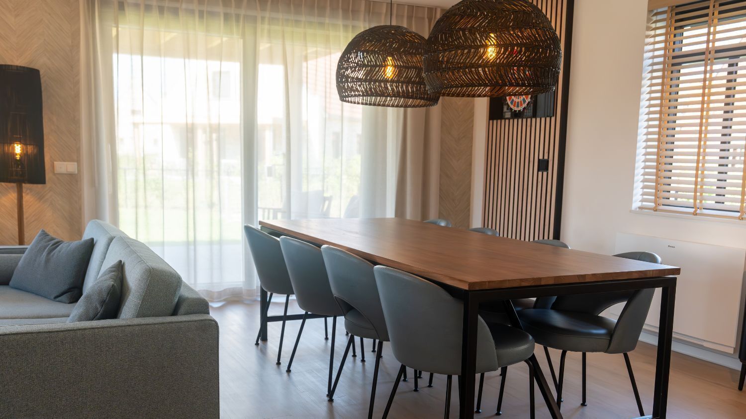 Un espace repas moderne avec une table en bois et des chaises grises, un canapé et une lampe fixée au mur.