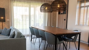 Un espace repas moderne avec une table en bois et des chaises grises, un canapé et une lampe fixée au mur.
