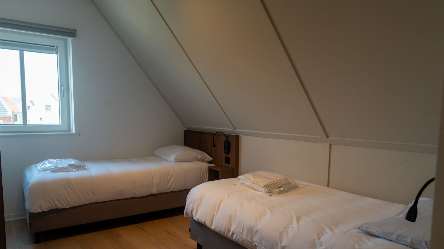 A bedroom with two single beds, a window, and a sloped ceiling.