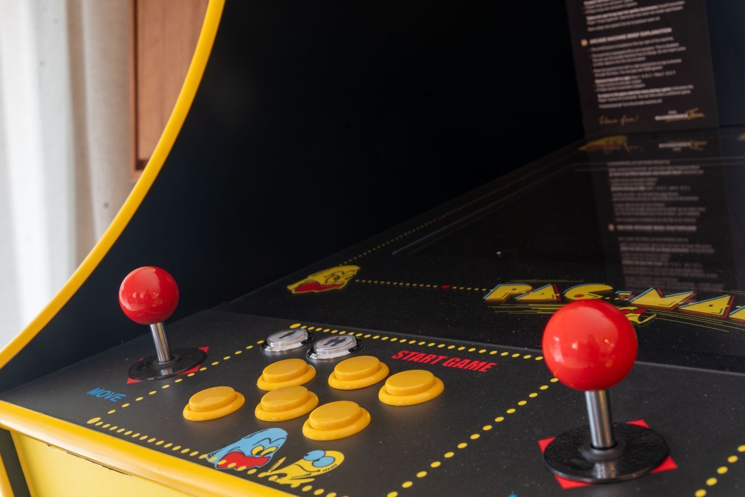 A Pac-Man arcade machine with yellow buttons and red joysticks.