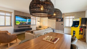Een moderne woonkamer met een houten eettafel, een bank, een aan de muur bevestigde televisie en een gameconsole.