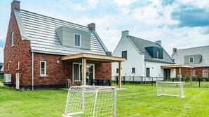 Zona residencial con dos casas, una de fachada de ladrillo y la otra con exterior blanco. Se ven dos porterías de fútbol en primer plano.