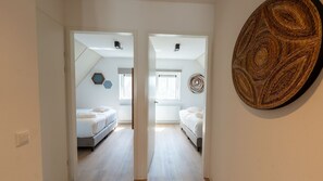 Un couloir menant à une chambre à coucher, qui contient un lit, une porte et une œuvre d’art accrochée au mur.