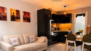 Una sala de estar moderna con sofá, mesa de comedor, sillas, área de cocina y obras de arte en la pared.