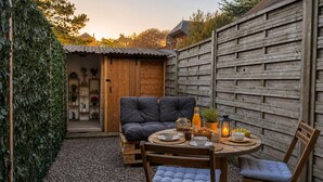 Un rincón exterior acogedor con una mesa redonda, dos sillones mullidos y un banco de madera.