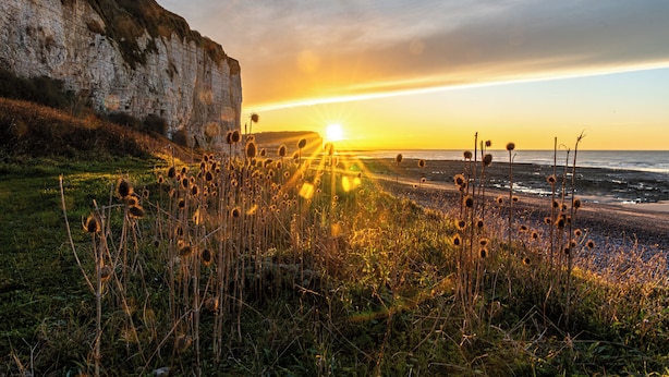 Un paisaje costero con acantilados y un atardecer sobre el mar.