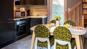 Cocina moderna con comedor, que incluye microondas, horno y lavamanos. Hay cuatro sillas con un estampado amarillo y negro, y una mesa preparada para dos.