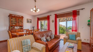 A living room with a sofa, striped armchair, dining table, and a wooden cabinet. - Country House 'Ivone' with Sea View, Private Pool and Wi-Fi (Portimão)