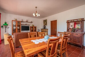 Ein Essbereich mit Holztisch, Stühlen, einer Couch, einem Fernseher und einer Kommode mit Dekoration.