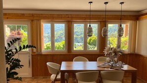 Ein Essbereich mit Holztisch und Stühlen, großen Fenstern mit Blick ins Grüne und hängenden Pendelleuchten.