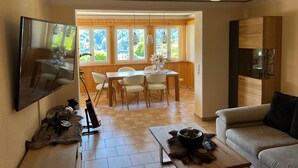 Ein modernes Wohnzimmer mit Flachbildfernseher, einem Essbereich mit Holztisch und Stühlen, einer Couch und einer ungewöhnlichen Deckenleuchte.