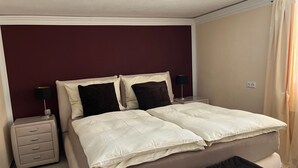 Ein Schlafzimmer mit einem Bett, zwei Nachttischen, einem Beistelltisch, einer schwarzen Tagesdecke und einer Wandsteckdose.