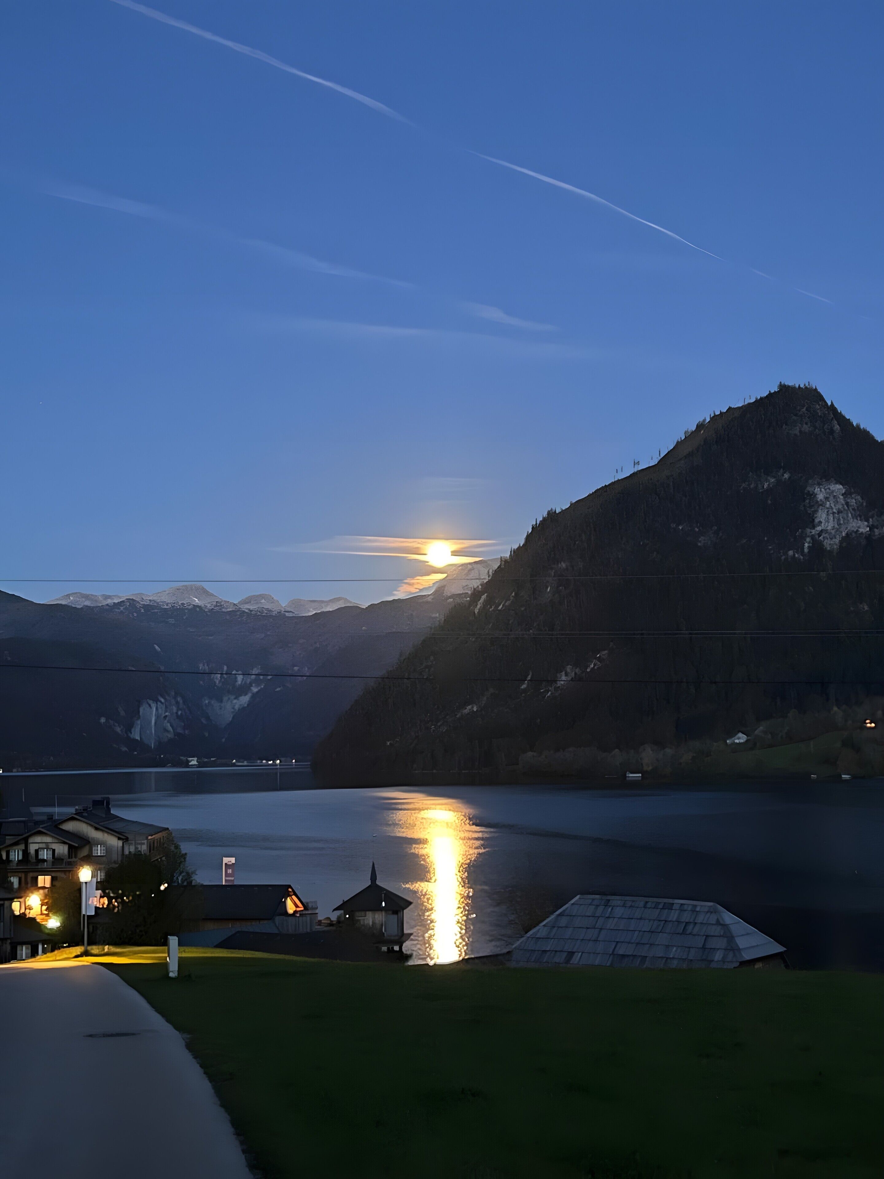 Berglandschap met een meer, een huis met een verlichte veranda, en een heldere lucht.
