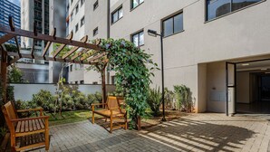 Une cour dotée d’une pergola en bois, de deux bancs en bois et d’un petit espace jardin agrémenté d’une plante grimpante.