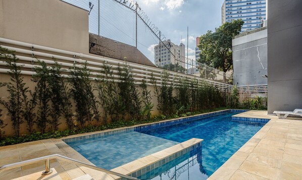 A rectangular swimming pool with a tiled edge, surrounded by a concrete deck and a low wall with climbing plants.