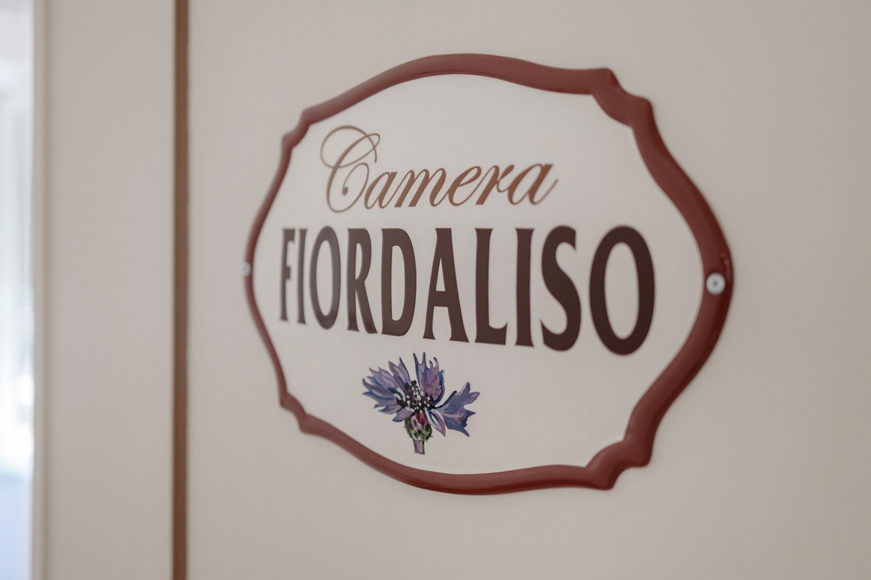 Een bord met de tekst 'Camera Fiordaliso' en een bloemendecoratie.
