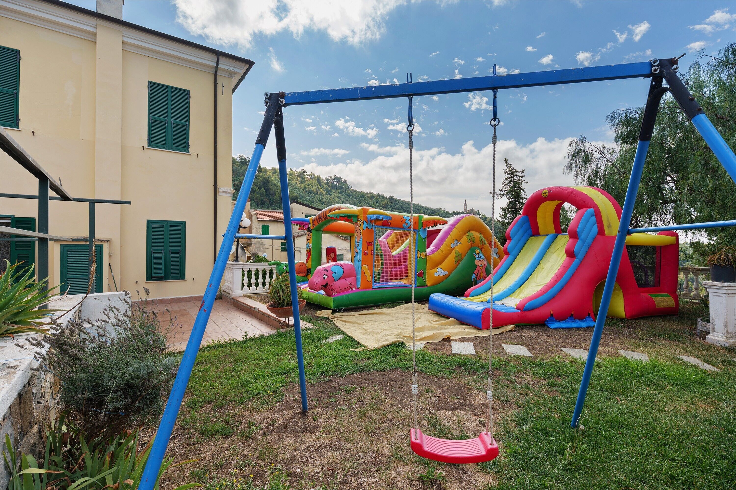 A residential area with a swing set, an inflatable slide, and a house with green shutters.