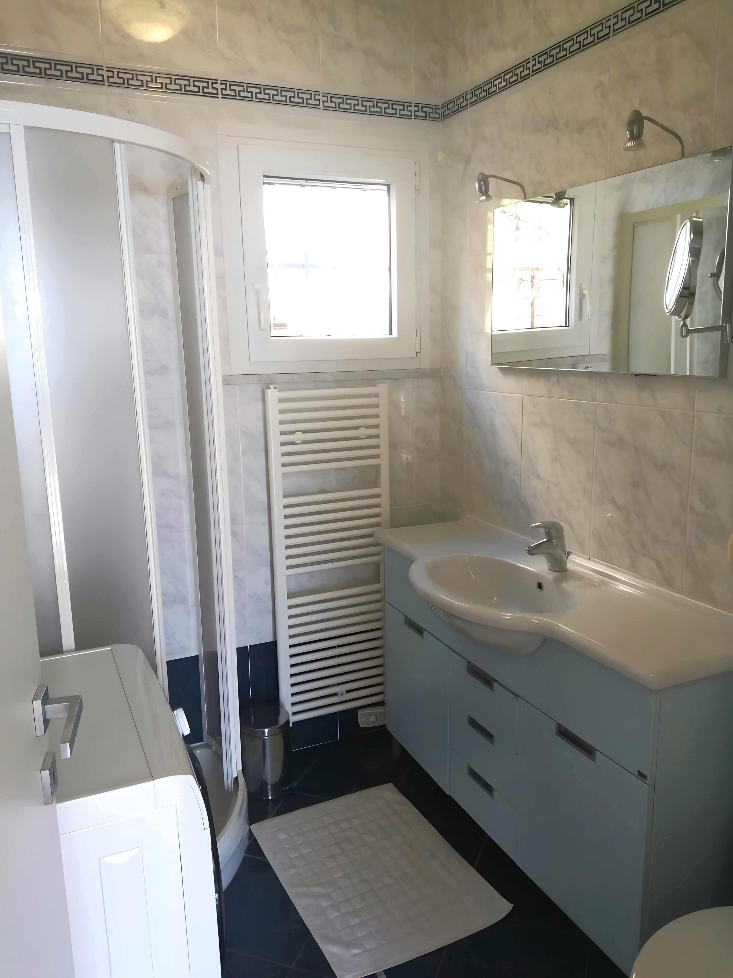 Une salle de bain avec un lavabo blanc, un miroir et une fenêtre située au-dessus du miroir.
