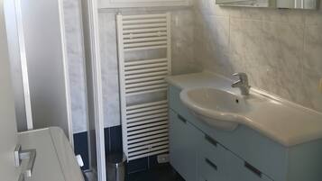 Une salle de bain avec un lavabo blanc, un miroir et une fenêtre située au-dessus du miroir.