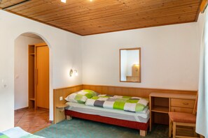 Un dormitorio con techo de madera, una cama con colcha a cuadros, una mesita de noche, un escritorio de madera y un espejo en la pared.