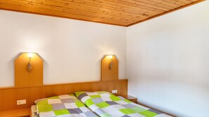 A room with a wooden ceiling, two bedside lamps, a bed with a checkered bedspread, and a nightstand. - Room '5' with Mountain View, Shared Terrace and Wi-Fi (Hopfgarten in Tirol)