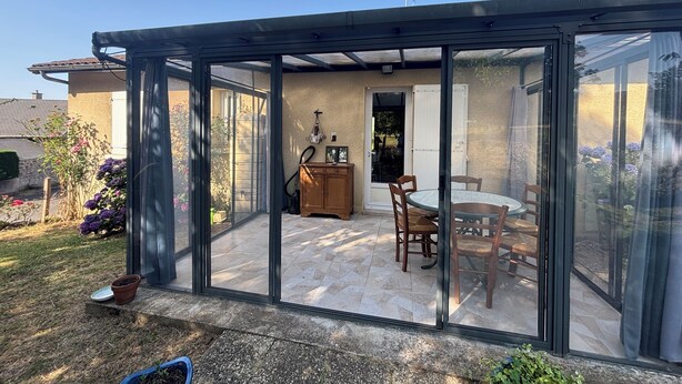 Een glazen patio met een tafel, stoelen, een houten kast en een deur naar een tuin.