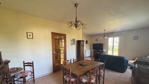 Een eetgedeelte met een houten tafel en stoelen, een kroonluchter, een klok en een televisie op de achtergrond.