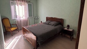 Een slaapkamer met een bed, een stoel, een nachtkastje en een raam met gordijnen.