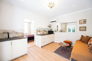 A modern kitchen with white cabinets, a marble backsplash, and a dining area with a round table and orange ottoman. - Charming house - L'Abricotier (Calvi)