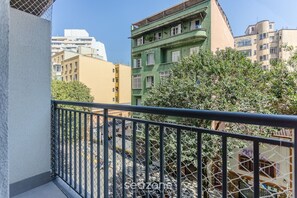 Ein Balkon mit Metallgeländer, der auf eine Straße mit Gebäuden und Bäumen blickt.