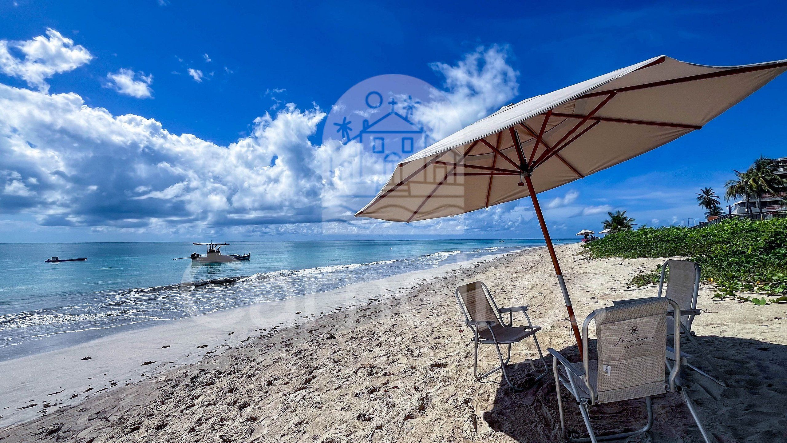A beach with a large umbrella, two beach chairs, and a boat in the water.