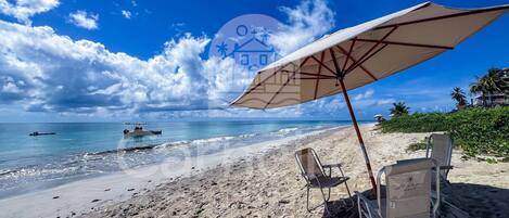 A beach with a large umbrella, two beach chairs, and a boat in the water.