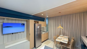 Una cocina moderna con refrigerador empotrado, un área de comedor con una mesa preparada para dos personas, y un televisor de pantalla plana montado en la pared.