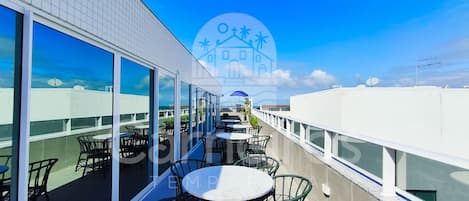 A rooftop terrace with outdoor seating, large windows, and a clear view of the sky.