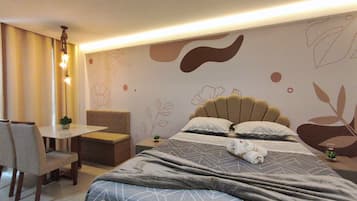 Quarto de hotel com cama, uma pequena mesa, uma cadeira e um detalhe decorativo na parede.