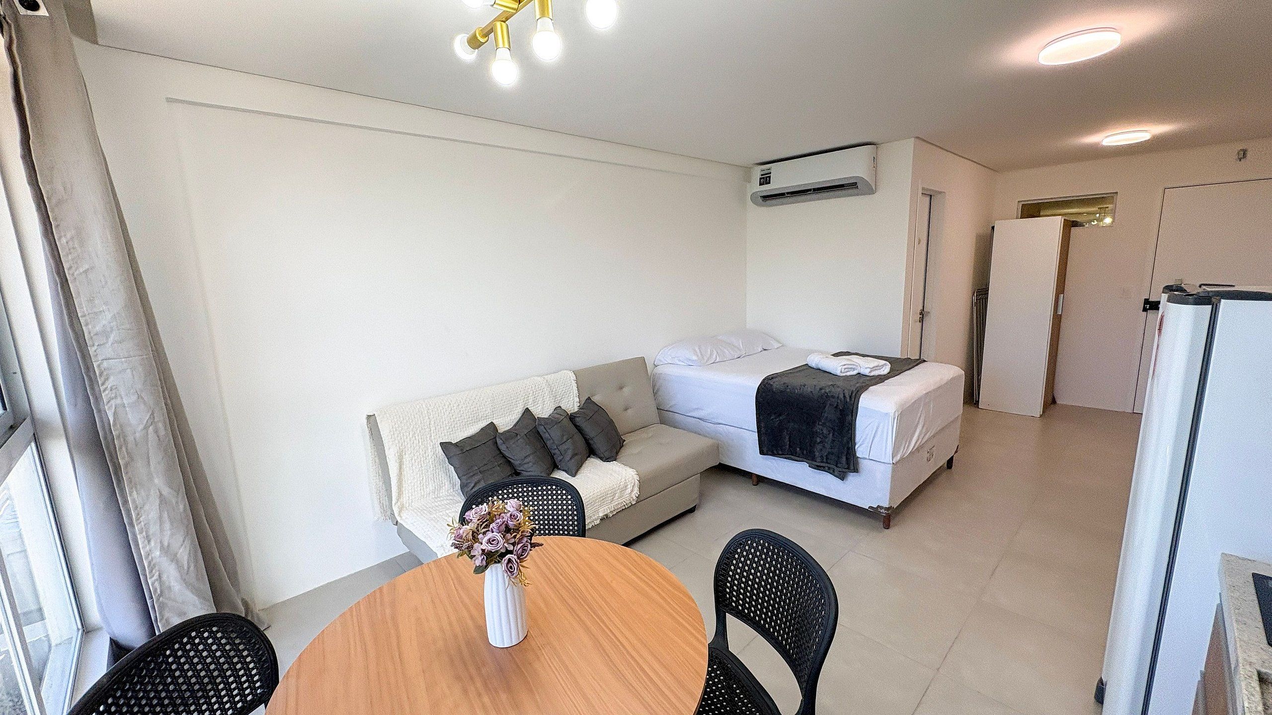 Quarto de hotel compacto com sofá, cama, mesa de jantar com cadeiras e ar condicionado.
