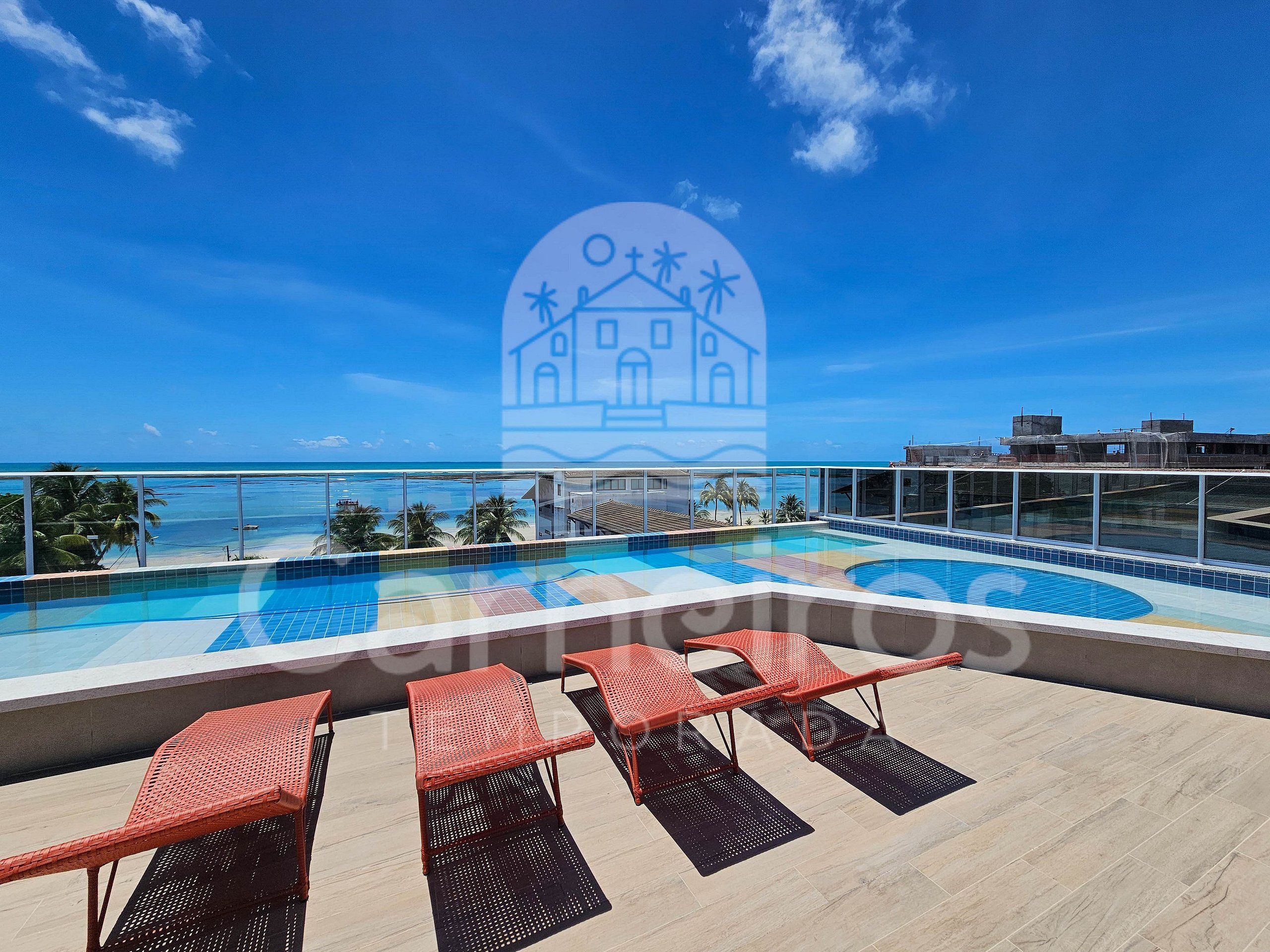 Piscina no terraço com espreguiçadeiras, vista clara do oceano e um edifício ao fundo.