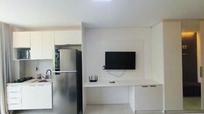 Eine moderne Küche mit weißen Schränken, einem integrierten Kühlschrank, einem flachbildfernseher an der Wand und einer kleinen Arbeitsplatte mit Spüle.