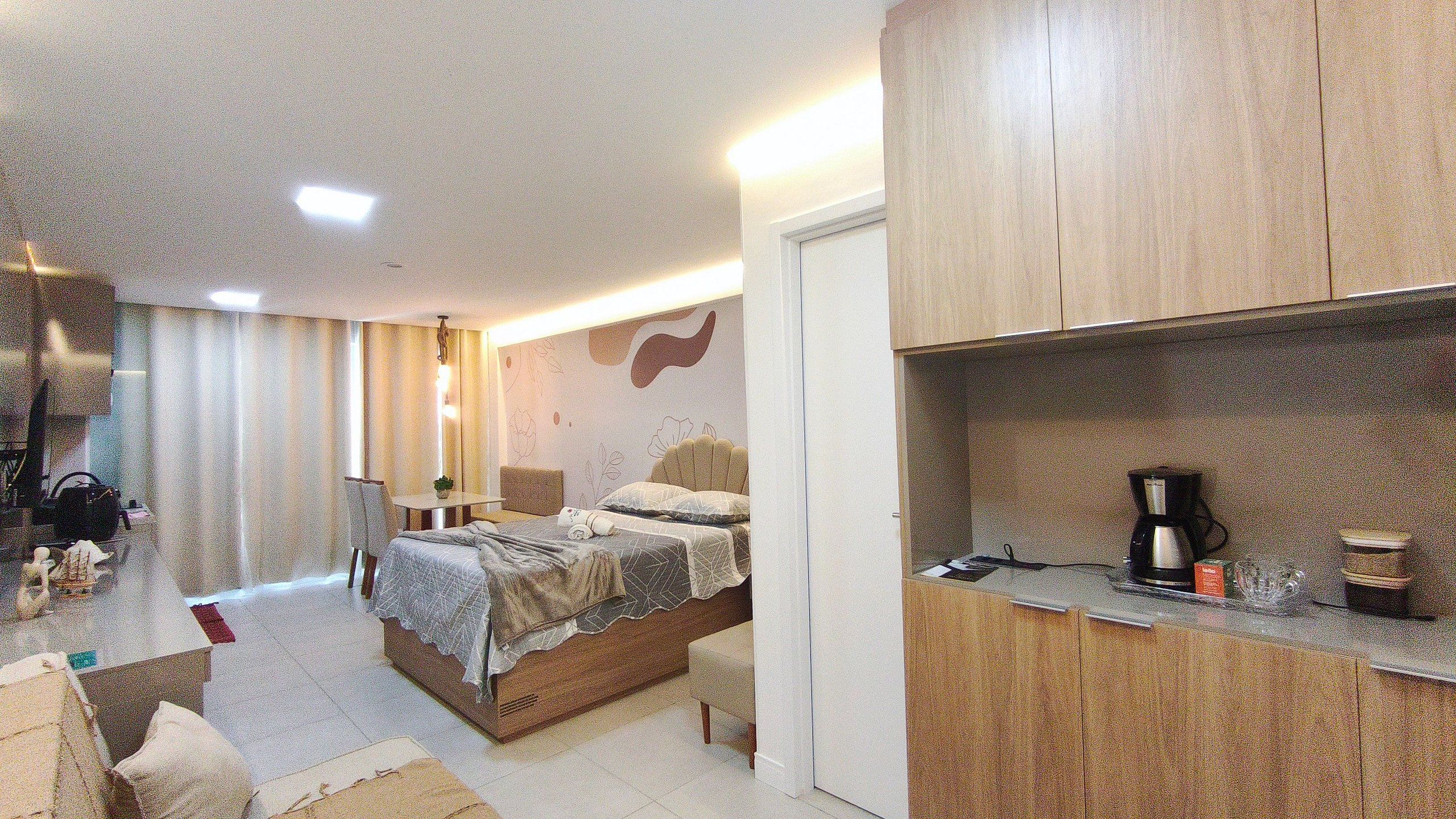 A hotel room with a bed, a small table, a chair, a desk, a coffee maker, and a cabinet.