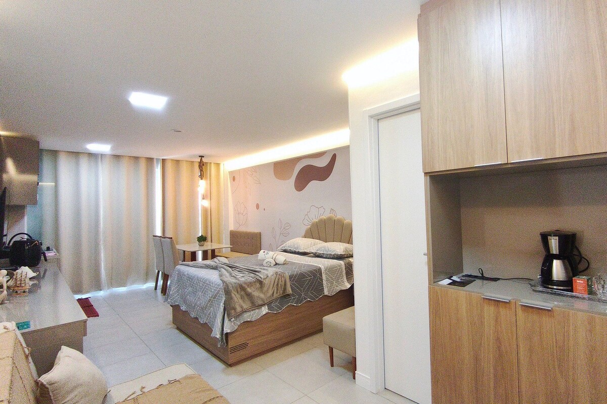 Una habitación de hotel con cama, una mesita, una silla, un escritorio, una cafetera y un armario.